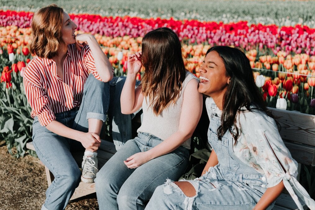 Three students sitting near a tulip field in the spring laughing
